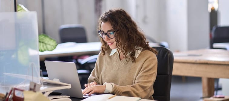 Young happy professional business woman employee sitting at desk working on laptop